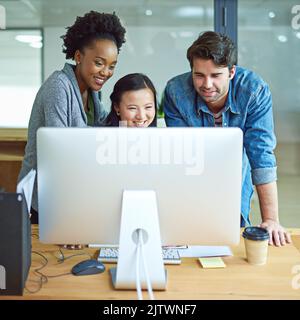 Three heads are better than one. a group of creative businesspeople gathered around a computer in the office. Stock Photo