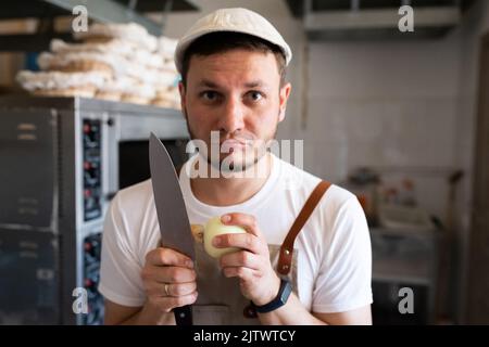 A baker is peeling onions in a small artisan bakery. Front view. Stock Photo