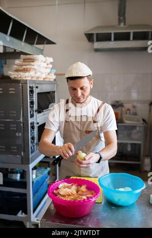 A baker is peeling onions in a small artisan bakery. Front view. Stock Photo