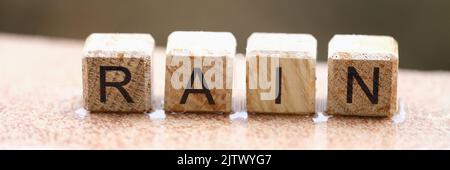 Wooden cubes with words rain lying on wet windowsill closeup Stock Photo