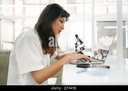 Young scientist in white lab coat working with binocular microscope in the material science lab Stock Photo