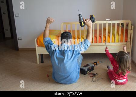 father and daughter celebrating after assembling the bedroom bed. Household do-it-yourself work Stock Photo