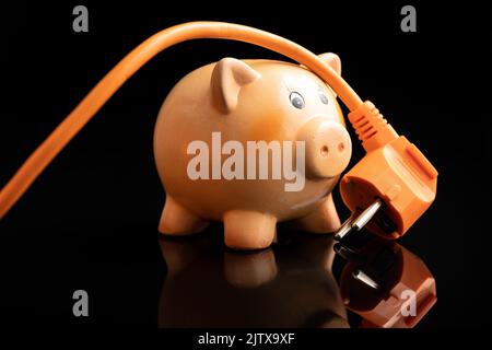 Orange electric plug and piggy bank on the black background. Concept of increasing electricity prices. Stock Photo