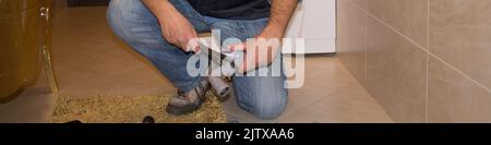 Hands of a plumber holding a wrench to tighten the pipes of a water tap. Horizontal banner Stock Photo