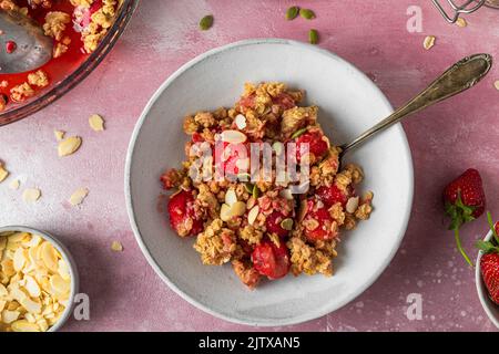 Delicious strawberry crumble with almonds and pumpkin seeds in a plate on pink background. Top view. Tasty breakfast Stock Photo