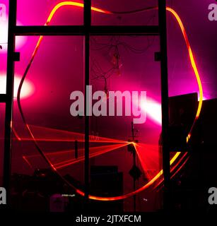 Red deformed neon with laser lights flashing behind the strange shape seems the interior of an alien ship. Wires hang inside a seemingly UFO craft Stock Photo