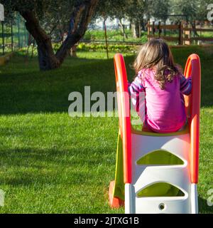 adorable little girl playing in the garden on the slide Stock Photo