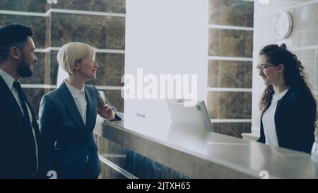 Receptionist talking with arrived businessman and businesswoman guests about check-in in hotel and giving key card from room to man . Business, travel and people concept Stock Photo