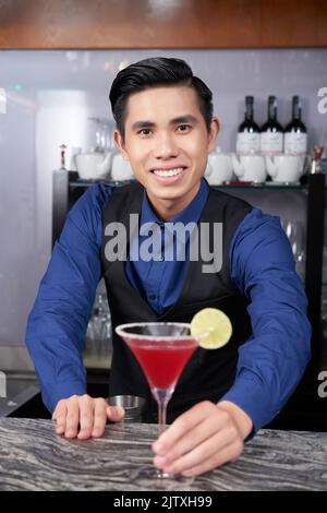 Cheerful young waiter offering young red margarita Stock Photo