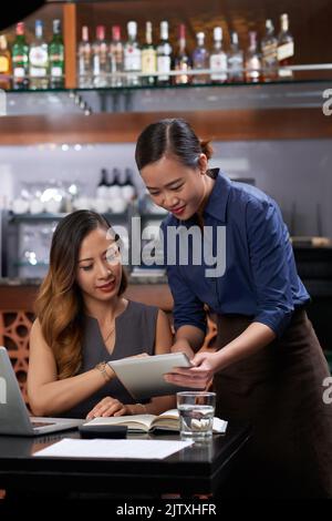Waitress showing menu on tablet computer to visitor Stock Photo
