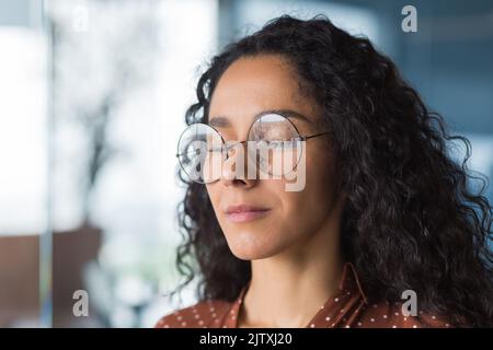 Closeup portrait female programmer engineer developer with closed eyes in glasses, dreaming and visualizing desired result, businesswoman working in modern office, Hispanic with curly hair in casual Stock Photo