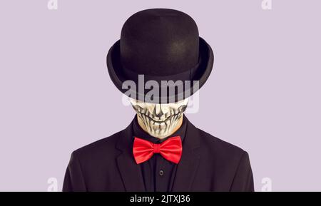Skeleton man in black suit and red bow tie hiding his Halloween skull face under black hat Stock Photo