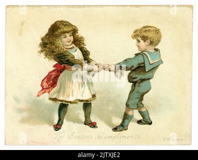 Original, charming Victorian Christmas card, greetings card of young Victorian boy and girl pulling a cracker. The boy is dressed in a sailor suit, the girl has long hair in waves, the caption is 'The Season's Compliments', dated 1887, U.K. Stock Photo