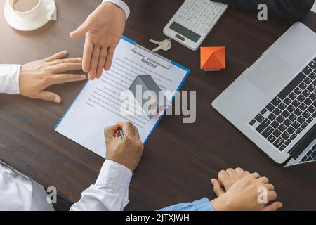 Home sales and home insurance concept. Real estate agent talked about the terms of the home purchase agreement and asked the customer to sign the docu Stock Photo