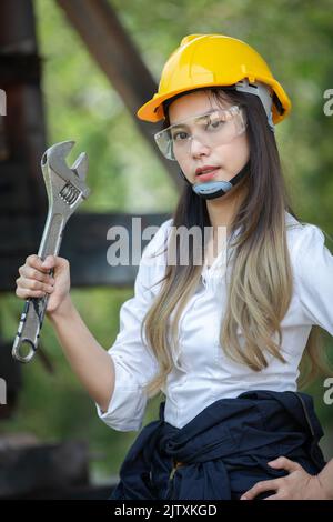 Female engineer smiling with yellow hard hat helmet and holding and holding a wrench. Stock Photo