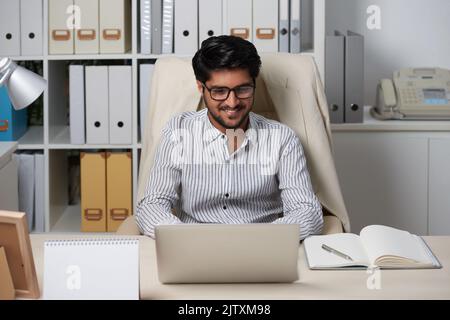 Cheerful young entrepreneur writing e-mails to business partners Stock Photo