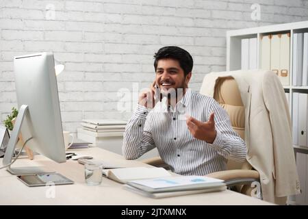 Handsome young Indian entrepreneur talking on phone to client or business partner Stock Photo