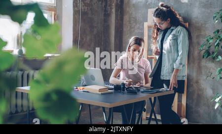 Young professional designer is discussing new project with female photographer choosing illustrations carefully. Busy day in designing company concept. Stock Photo