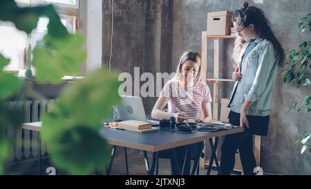 Young professional designer is discussing new project with female photographer choosing illustrations carefully. Busy day in designing company concept. Stock Photo
