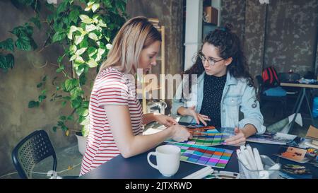 Attractive female designers are busy working with color palettes to determine colors on photograph. Work day in design company concept. Stock Photo