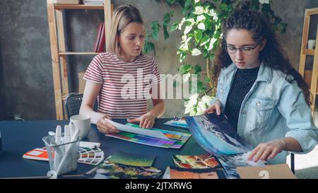 Creative designers are placing colourful photos on table and sharing ideas while sitting together in modern office. Creative thinking concept. Stock Photo