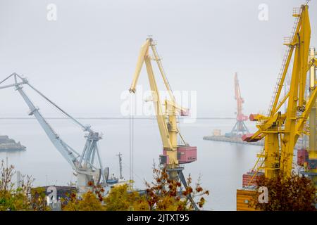 Odesa, Ukraine - OCT 22 2019: Autumn fog in the sea cargo port. Level luffing cranes and gantry cranes in the container terminal Stock Photo