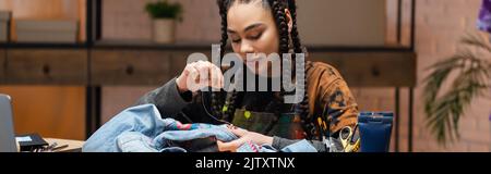 Young african american designer embroidering denim jacket in workshop, banner,stock image Stock Photo