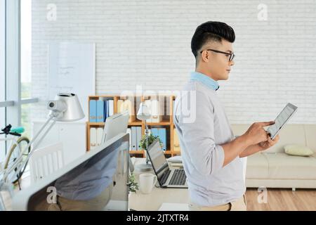Young manager standing at office and typing on touchpad Stock Photo