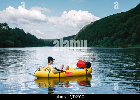 Tourist on yellow packraft rubber boat with red padle on a sunrise river. Packrafting. Active lifestile concept Stock Photo