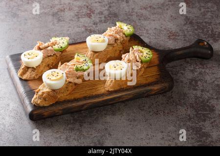 Healthy eating toasts with tuna, avocado and egg, with sesame seeds and olive oil closeup on the wooden tray on the table. Horizontal Stock Photo