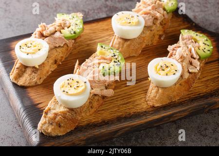 Avocado rye bread toast with tuna and boiled egg Healthy appetizer, breakfast, lunch or snack closeup on the wooden tray on the table. Horizontal Stock Photo