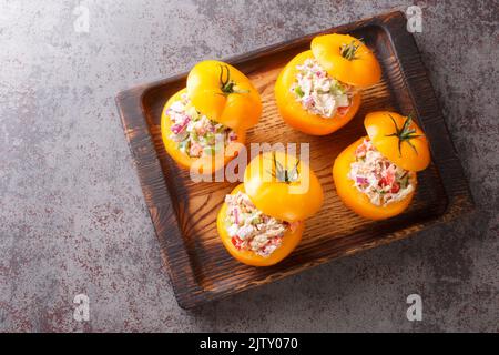Ripe tomatoes stuffed with a seasonal salad of canned tuna, bell peppers, onions and greens close-up on a wooden tray on the table. Horizontal top vie Stock Photo