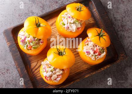 Tomatoes stuffed with a salad of canned tuna, bell peppers, onions and greens close-up on a wooden tray on the table. Horizontal top view from above Stock Photo