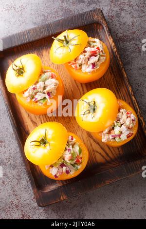 Traditional portuguese snack tomatoes stuffed with canned tuna and vegetables salad closeup on the wooden tray on the table. Vertical top view from ab Stock Photo