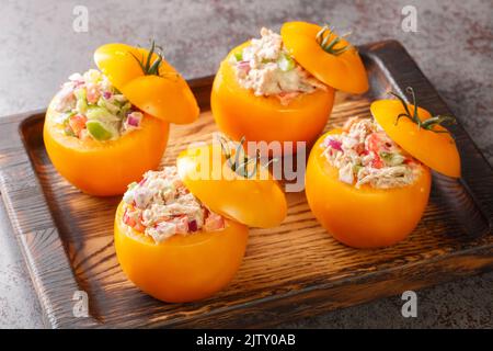 Tomatoes stuffed with a salad of canned tuna, bell peppers, onions and greens close-up on a wooden tray on the table. Horizontal Stock Photo