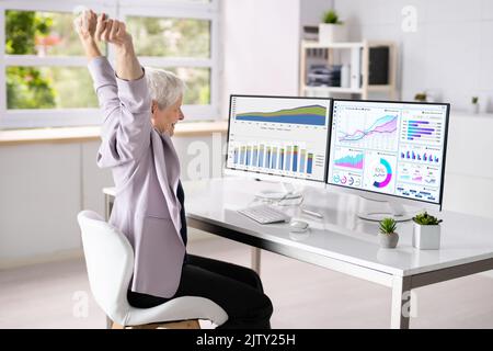 Excited Female KPI Data Analyst Using Multiple Screens Stock Photo
