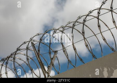 Chain link fence with barbed wire and razor wire. against the blue sky. Stock Photo