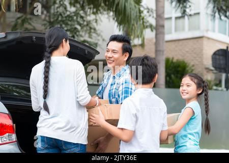 Happy family is standing near car with cardboard boxes Stock Photo