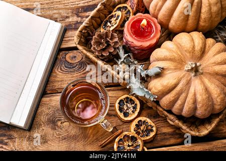 Cozy warm autumn composition with cup of hot tea, burning candle, open book and pumpkins on wooden background. Autumn home decor. Fall mood. Thanksgiv Stock Photo