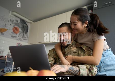 Asian woman in kitchen room hugging from back of military Stock Photo