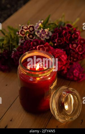 Yankee candle lit against a backdrop of flowers on a wooden board Stock Photo