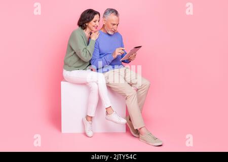 Full body photo of two idyllic partners sit podium use wireless tablet isolated on pink color background Stock Photo