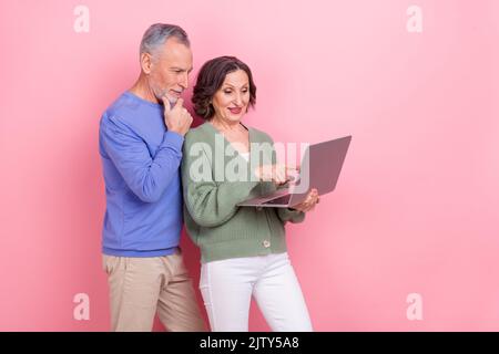Photo of two positive aged persons hold use wireless netbook isolated on pink color background Stock Photo
