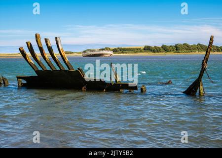 Remains of old wooden hull of a shipwreck with a more complete boat wreck across the bay. Traeth Dulas, Isle of Anglesey, North Wales, UK, Britain Stock Photo