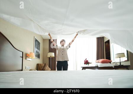 Smiling Asian maid putting fresh blanket on bed Stock Photo