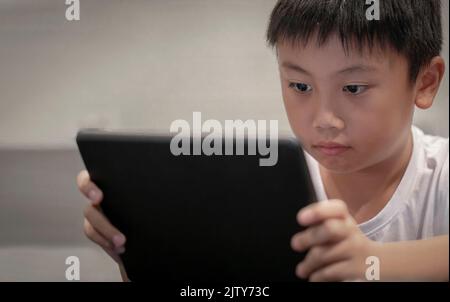 Asian boy playing game on digital tablet at home , Children watching cartoons on digital taplet or smartphone Stock Photo