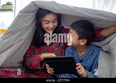 A happy asian family mother and son do activity together in living room playing game on digital tablet  and smiling happy while spending time together Stock Photo