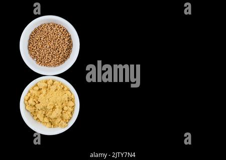 brown Mustard seeds and yellow mustard powder in white bowls on a black background Stock Photo