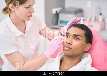 Experienced doctor preparing male client for cosmetic procedure Stock Photo
