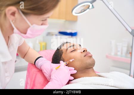 Female patient receiving cheek filler injection under skin of cheekbone ...